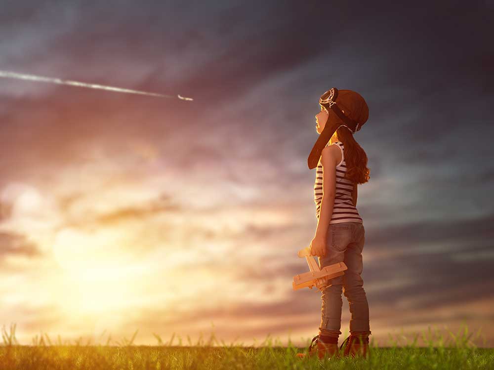 girl with airplane toy watches plane in the sky