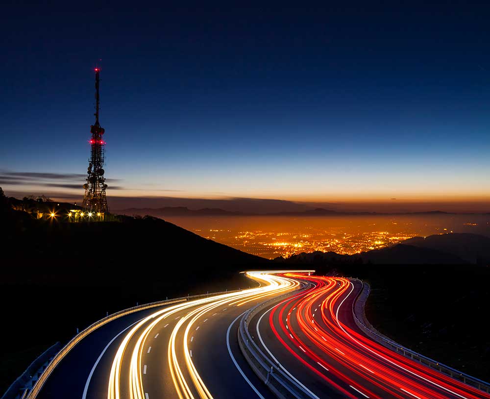 Car lights at night towards overexposed with city backdrop