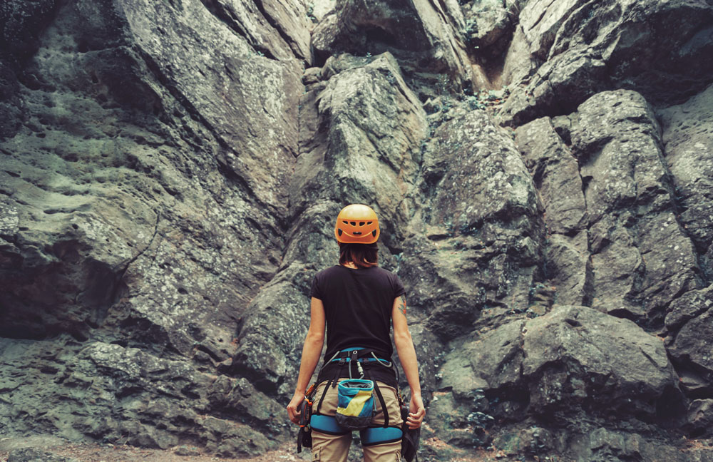 Female climber stands in front of rock wall