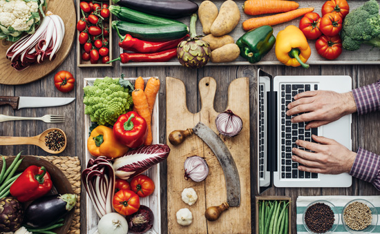 Table full of different foods and someone typing on a computer to represent globally sourced food