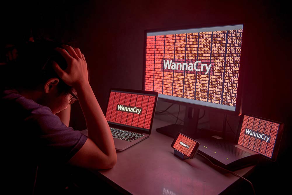 distressed man in front of 3 devices hacked with WannaCry virus
