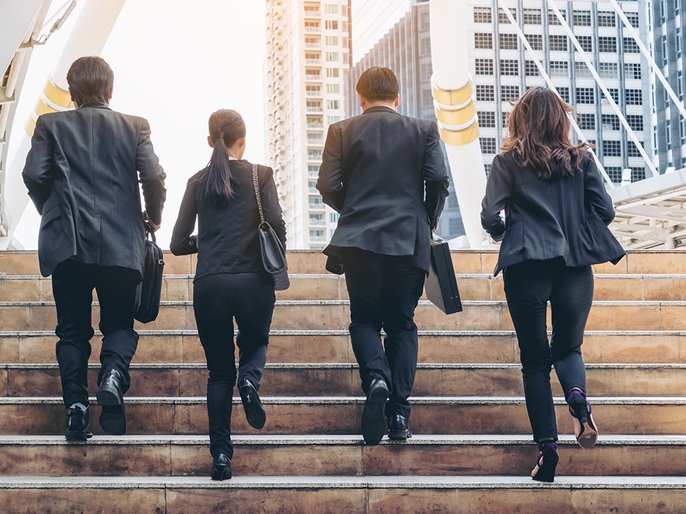 Lively business team running in the city. Group of businessmen and businesswomen wearing full business suit with business buildings background.