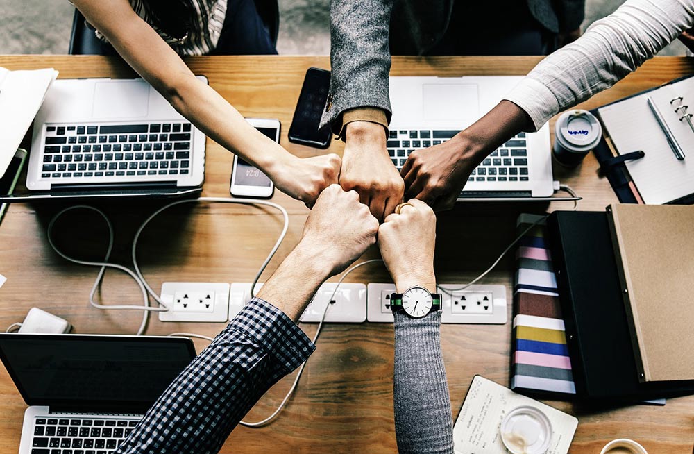 5 coworkers pounding fists over board room table