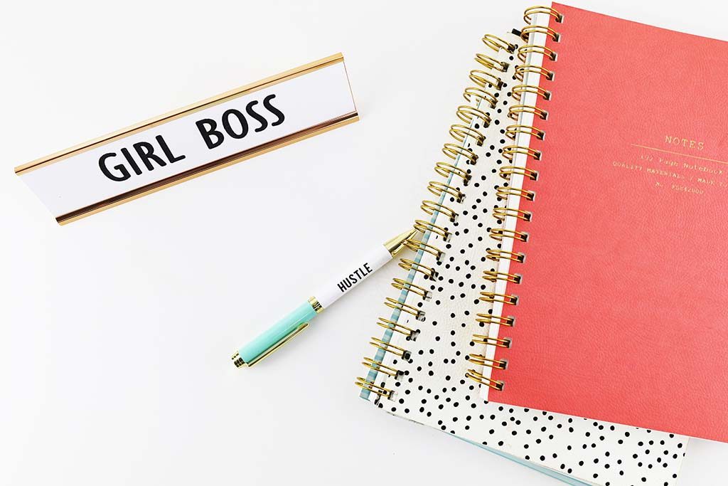 Notebooks and Girl Boss name plate on a white desk