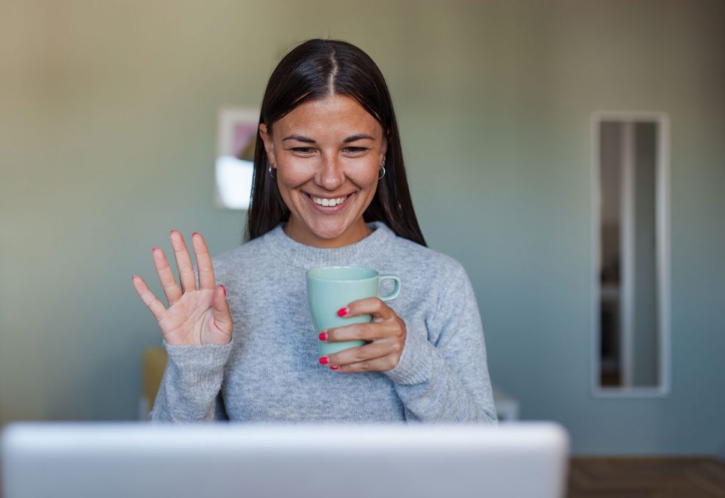 woman smiling and waving with coffee and laptop