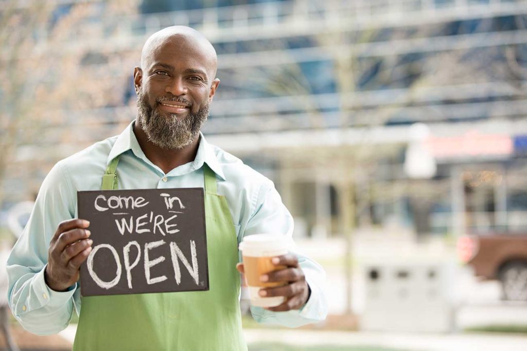 Business owner with open sign outside of coffee shop