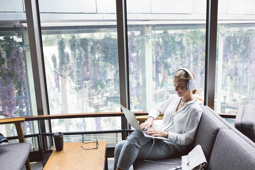 business woman on laptop with headphones on couch