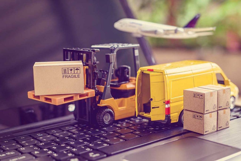 miniature forklift van and airplane on laptop keyboard delivering boxes