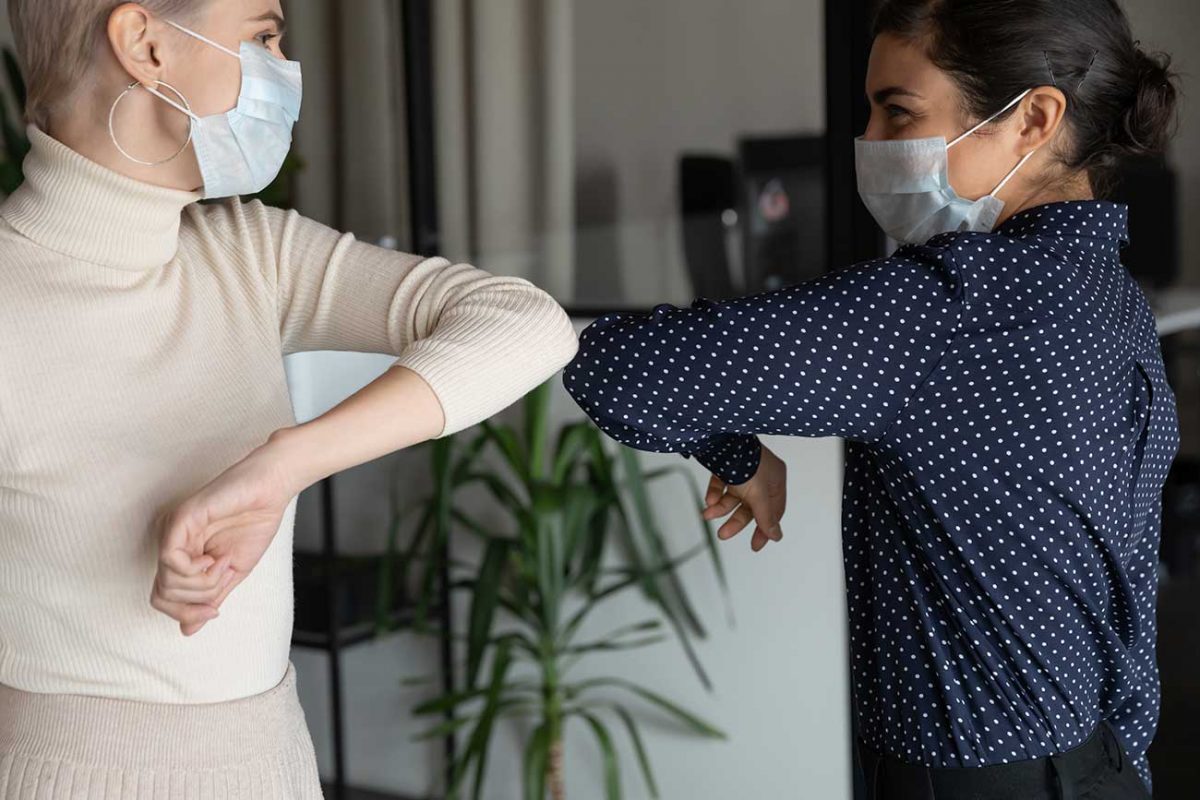 Two business women wearing masks and bumping elbows in celebration