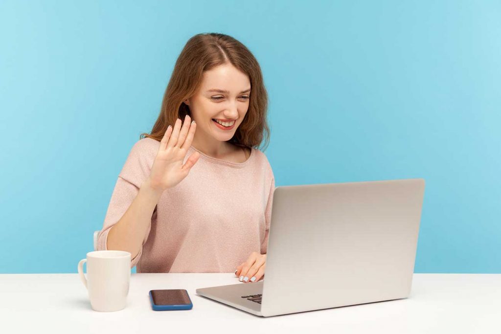 Young woman waving at laptop