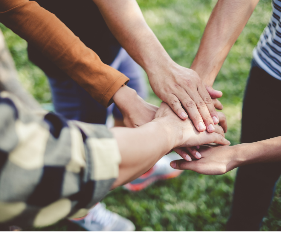 Group of people joining hands in the middle of a circle, denoting cooperation