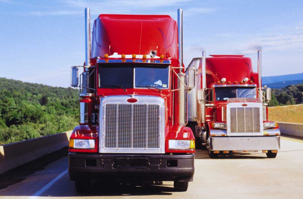 Two red transport trucks passing on a highway - representing digital freight and legacy freight companies.