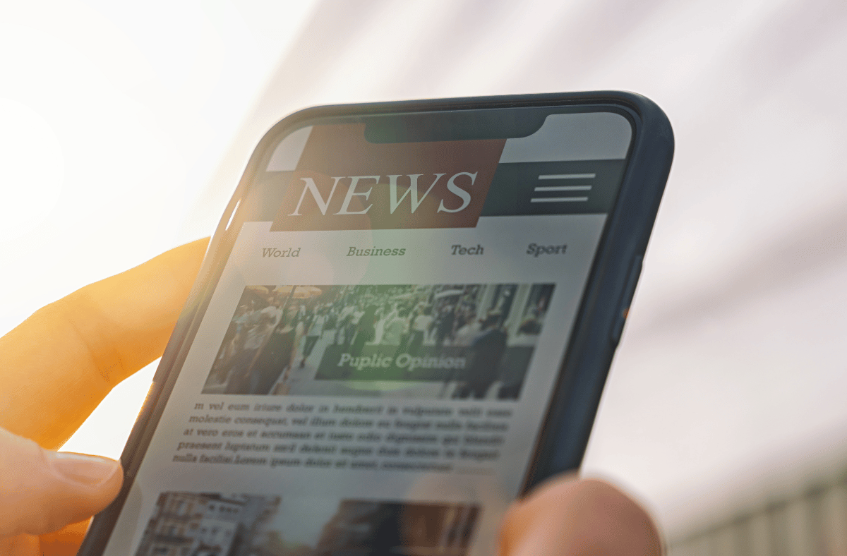 Hand holding a mobile phone with international trade news articles on the screen