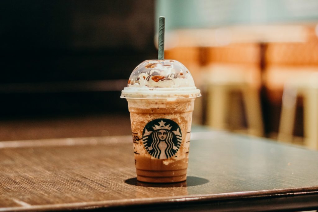 Starbucks Frappuccino on a wooden table inside a cozy coffee shop with blurred background